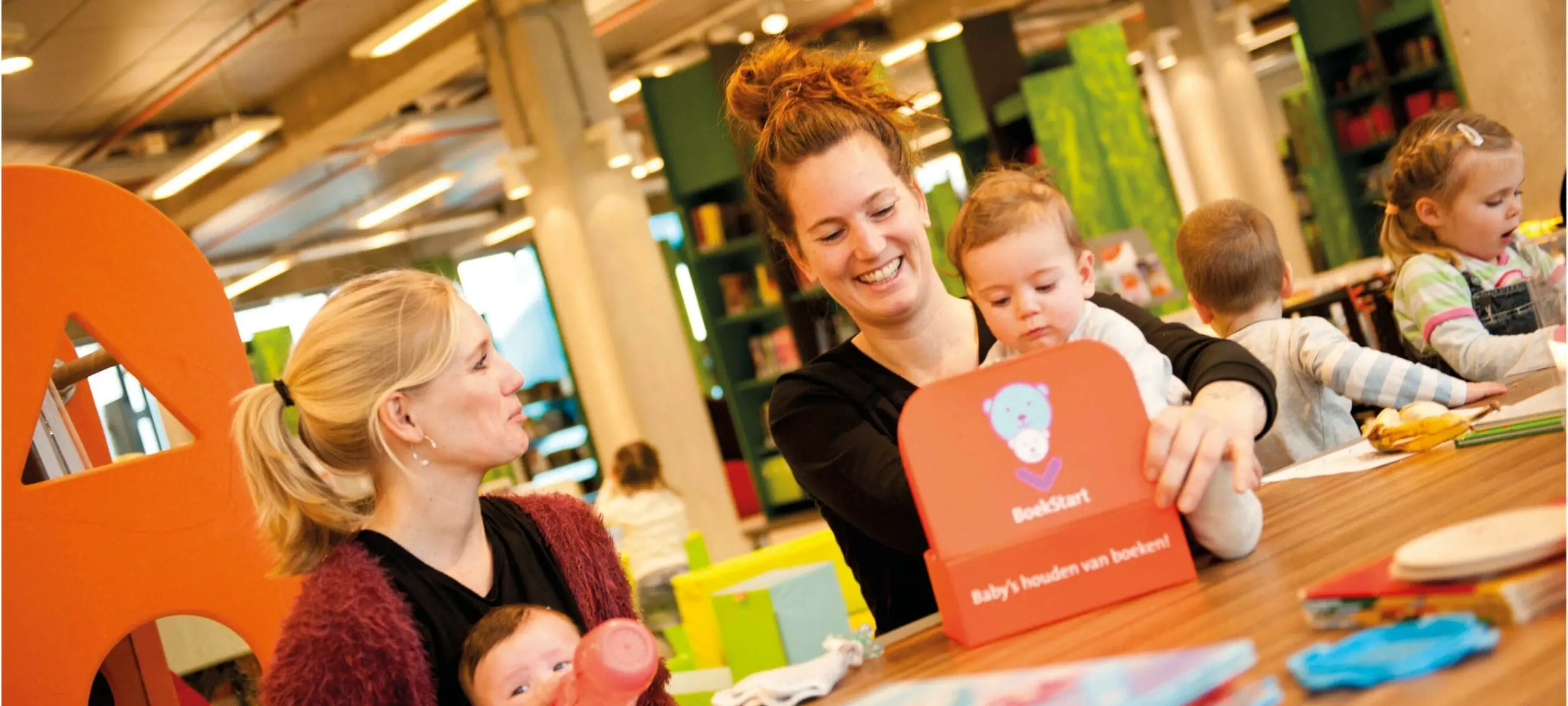 Twee moeders met een kindje halen hun BoekStartkoffertje op