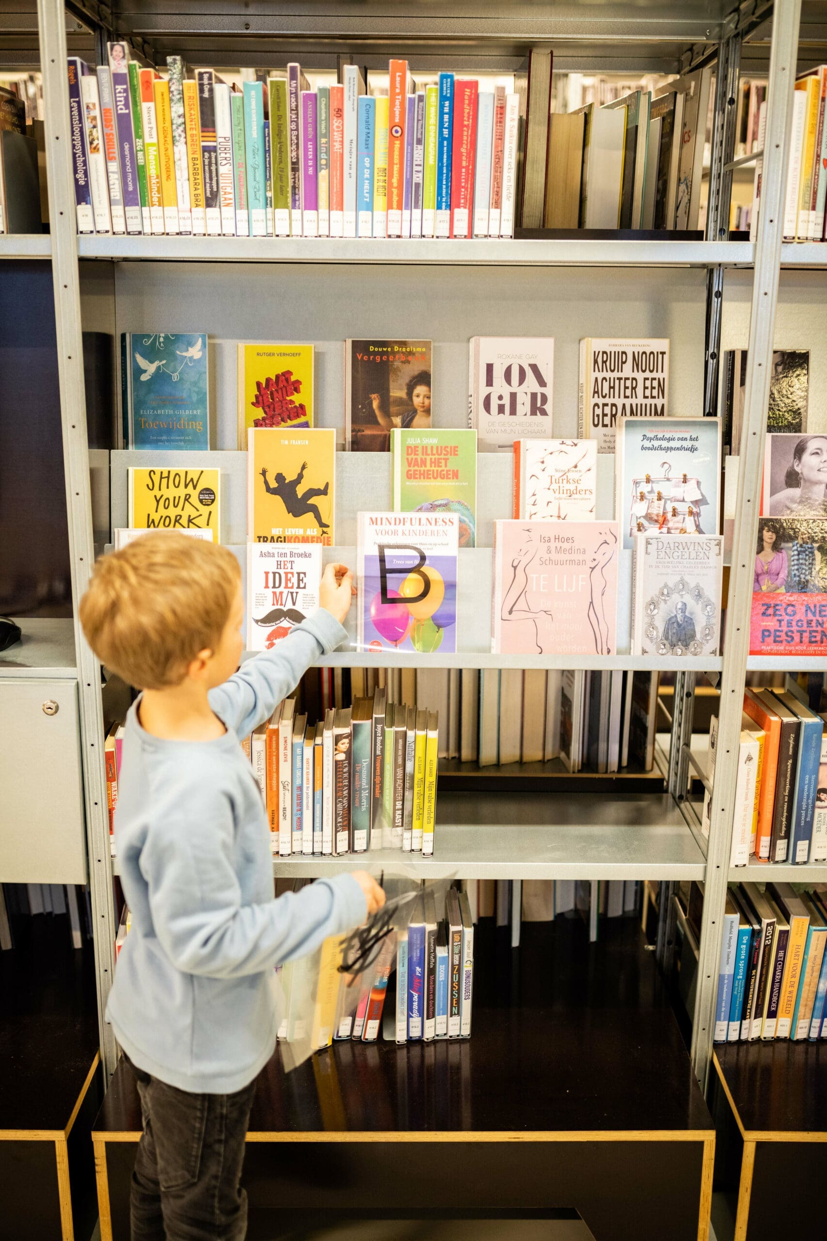 Een jonge jongen pakt een boek uit de boekenkast.