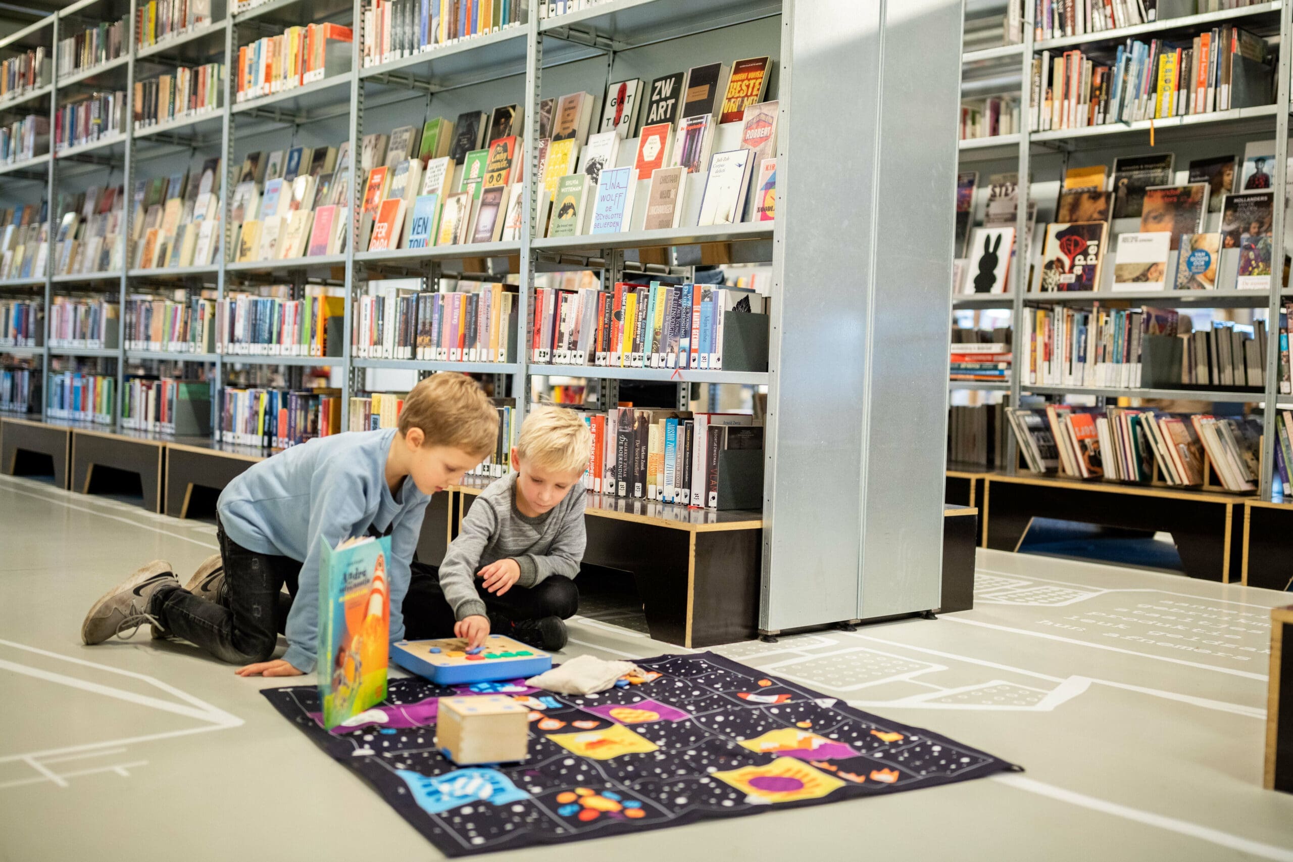 Twee jongens spelen op de grond van een bibliotheek met boekenkasten op de achtergrond