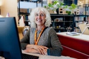 Een bibliotheekmedewerker kijkt lachend in de camera met haar armen over elkaar
