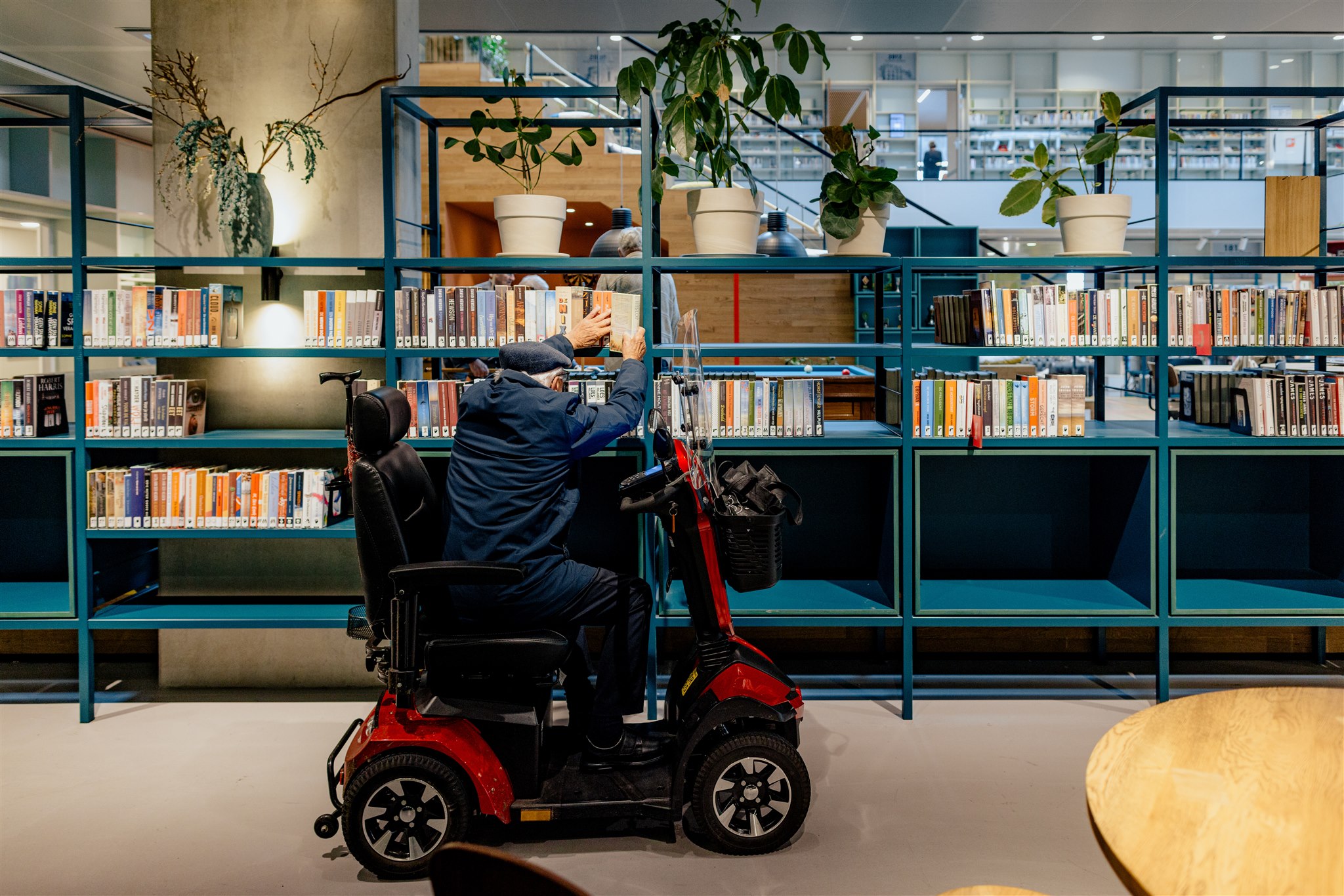 Bezoeker in scootmobiel pakt boek uit de kast in bibliotheek Eemnes