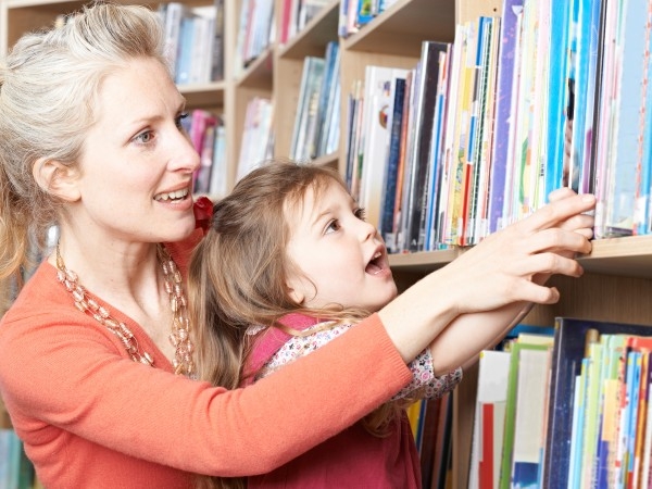 Een moeder zoekt met haar dochtertje naar een boek in een kast vol boeken.