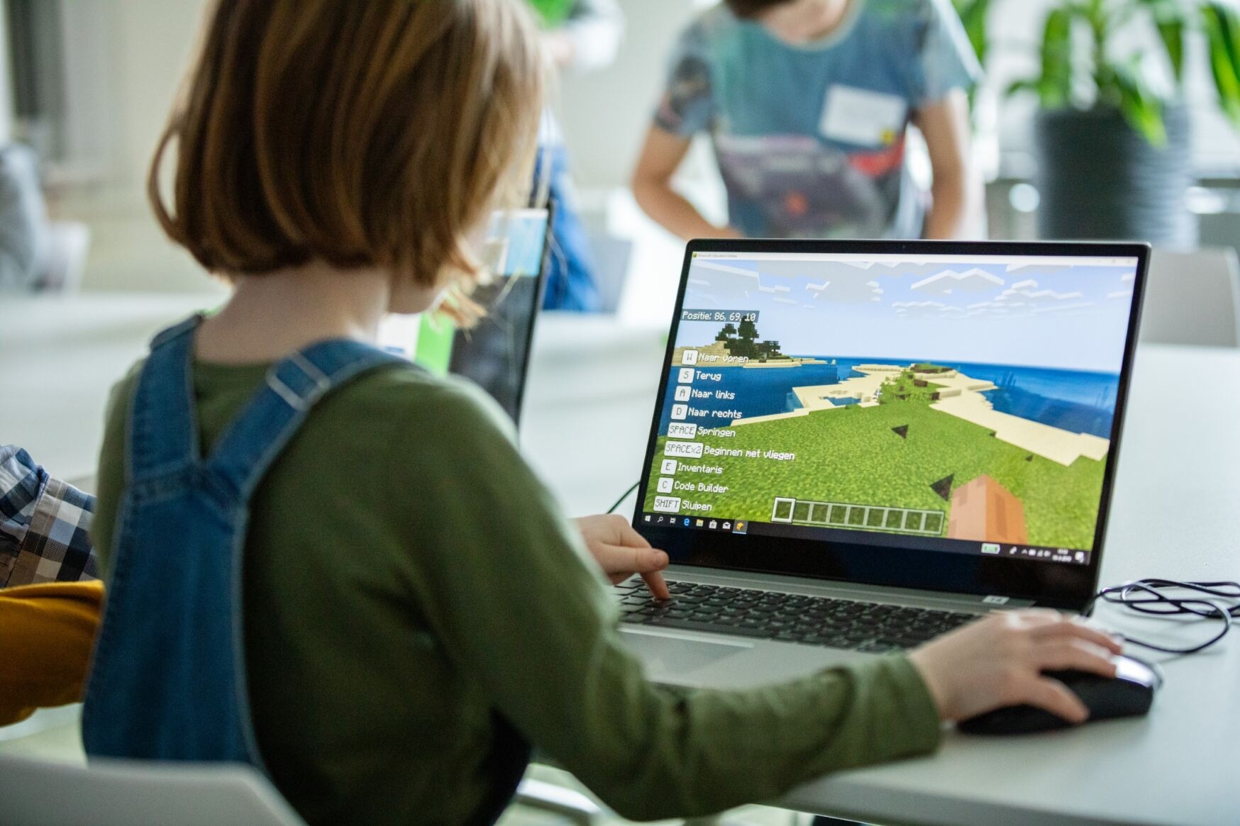 Een jong kind zit achter de laptop en speelt het spel Minecraft