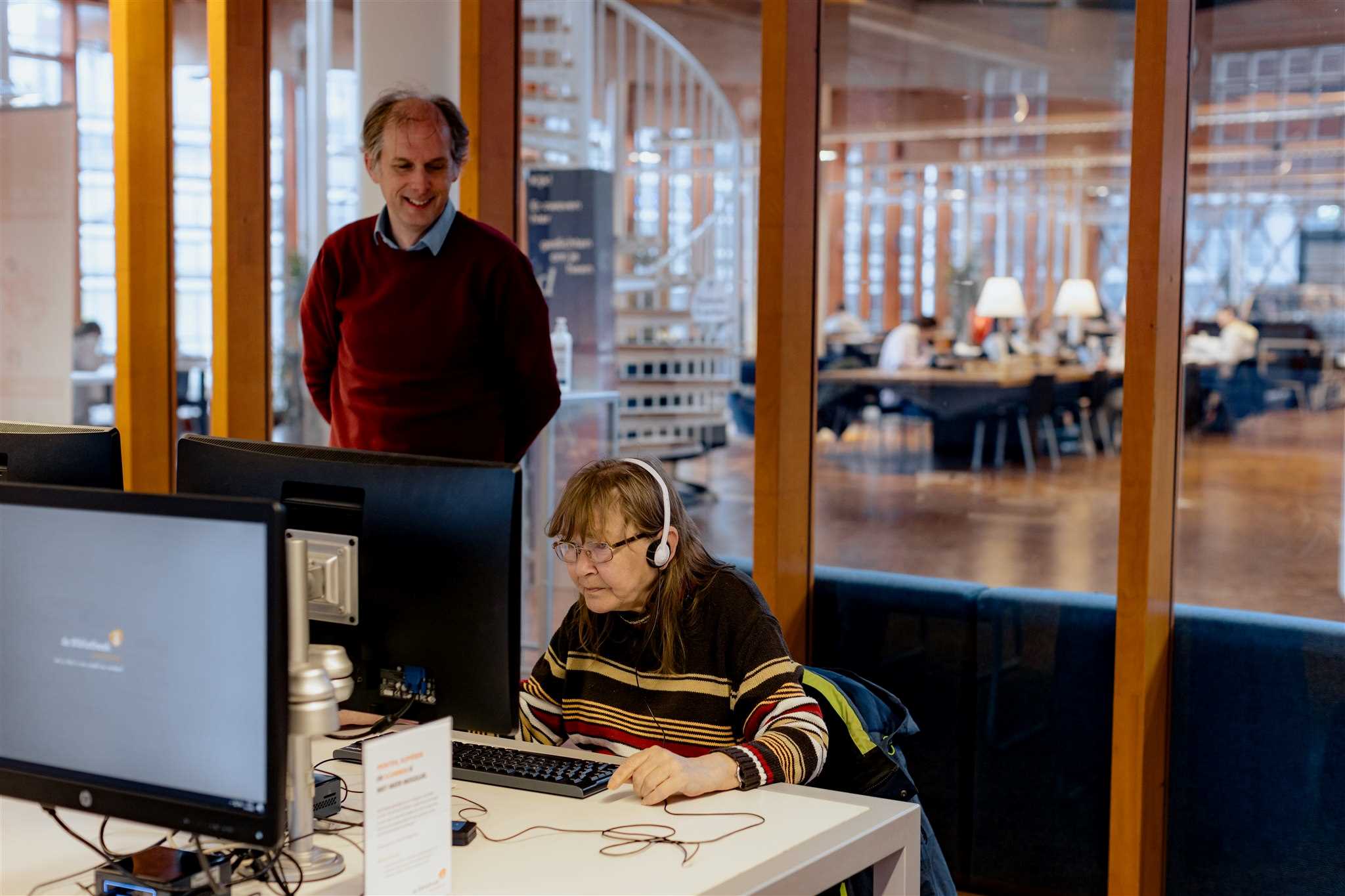 Een oudere dame leert te werken op een computer in de bibliotheek