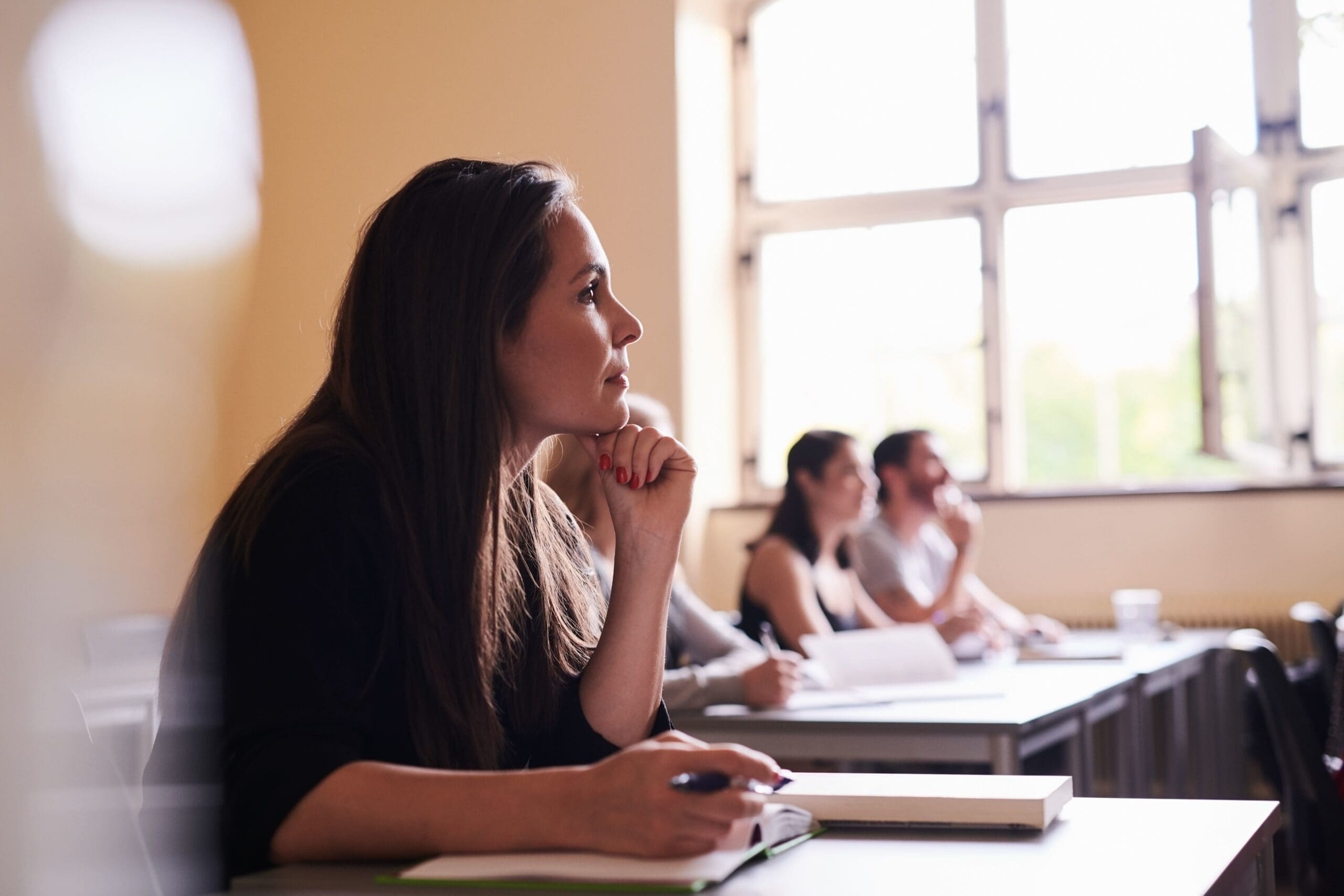 vrouw in schoolbankje dat oplettend zit te kijken met hand onder haar kin