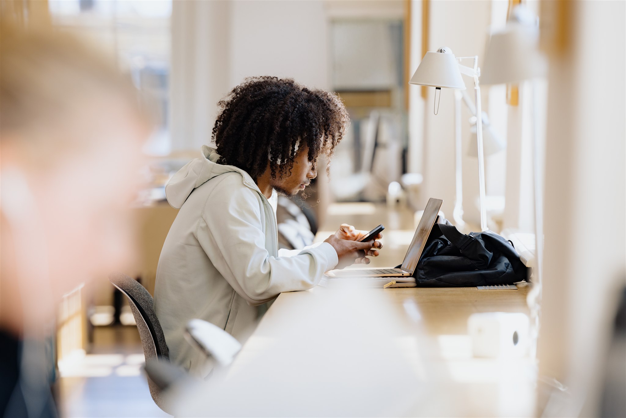 jongen zit in de bibliotheek op zijn telefoon