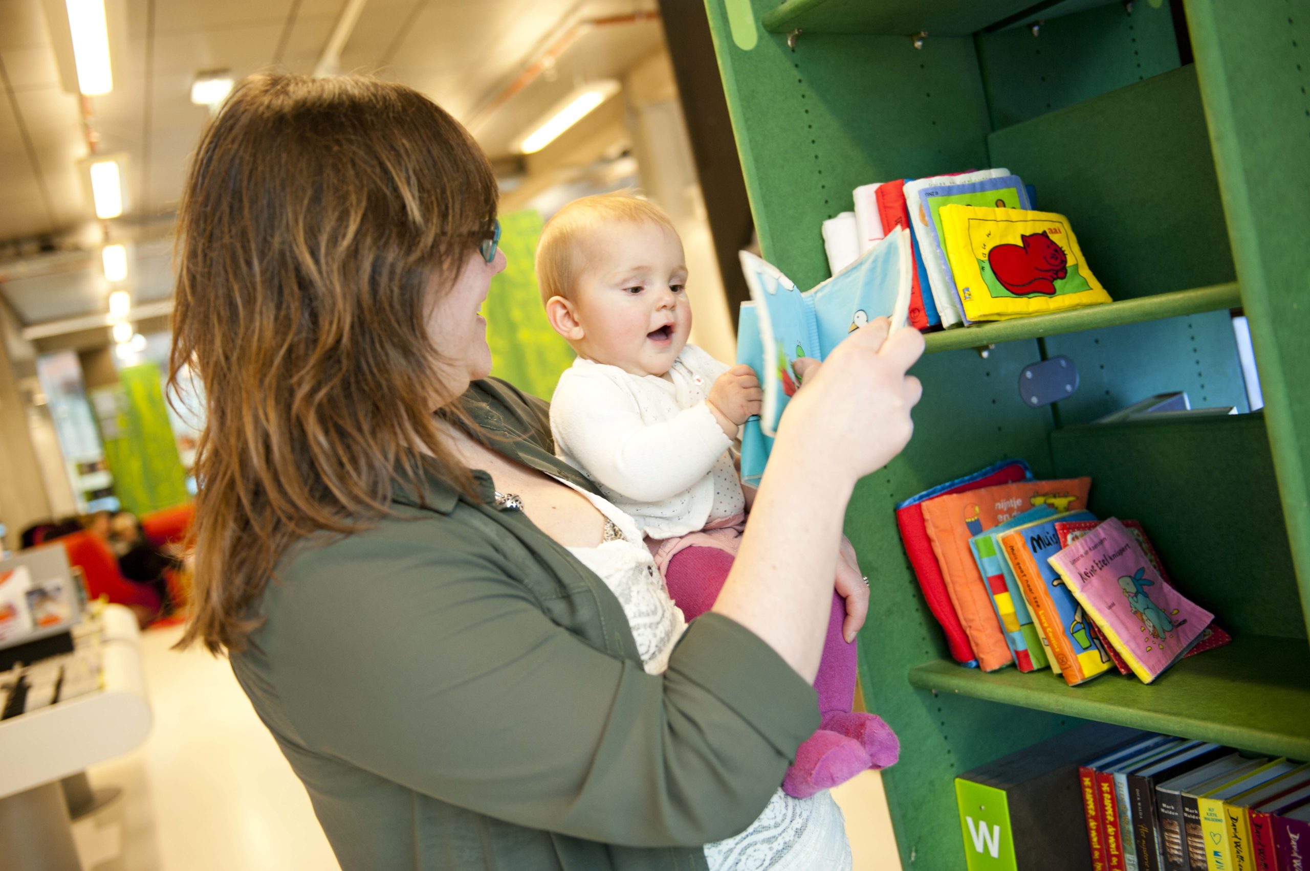moeder met kind op arm staat voor boekenkast in een bibliotheek