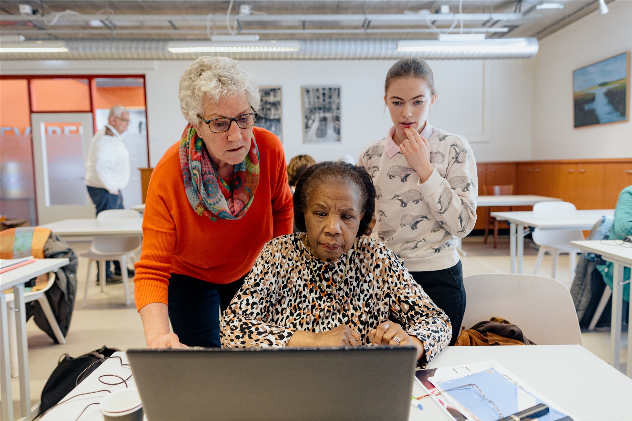 mevrouw zit achter laptop met 2 bibliotheekmedewerkers die meekijken en uitleg geven